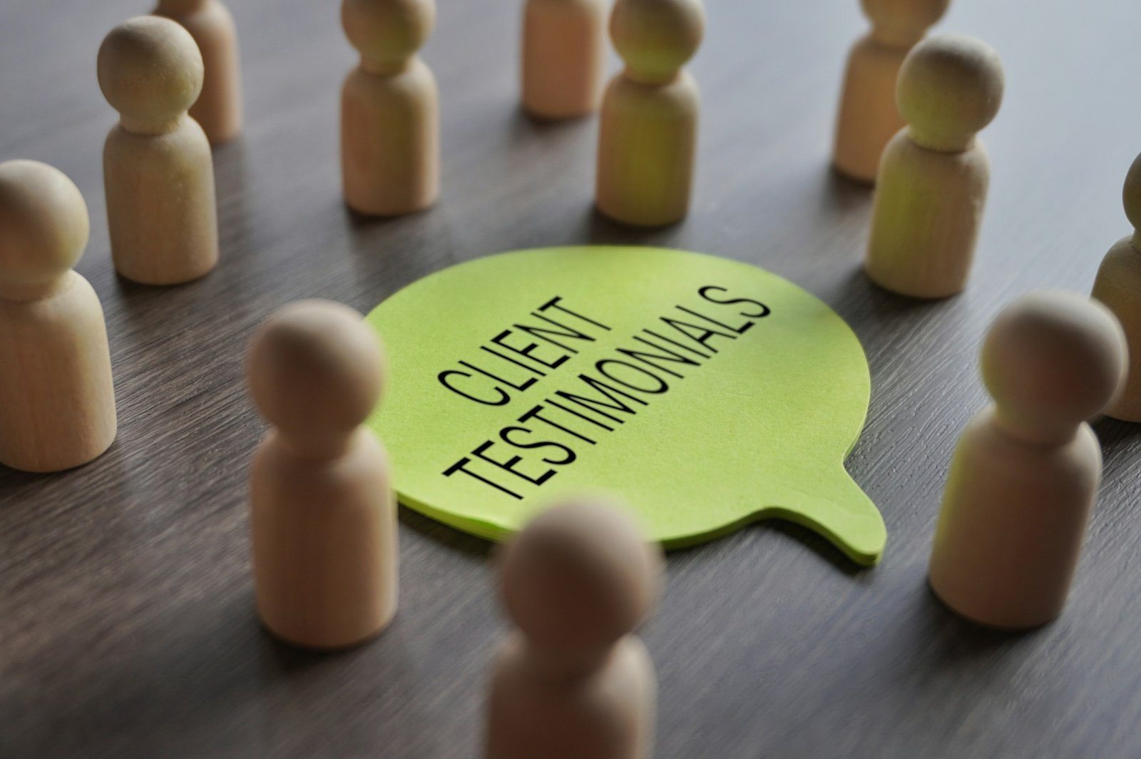 A group of wooden figurines surrounding a speech bubble with text CLIENT TESTIMONIALS.